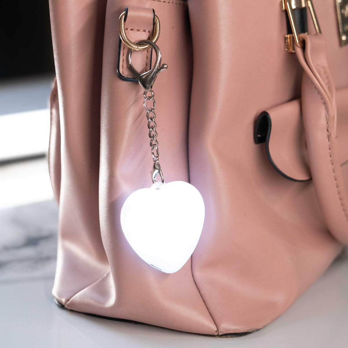 LumiHeart™ Motion Glow heart-shaped keychain light glowing softly attached to pink handbag
