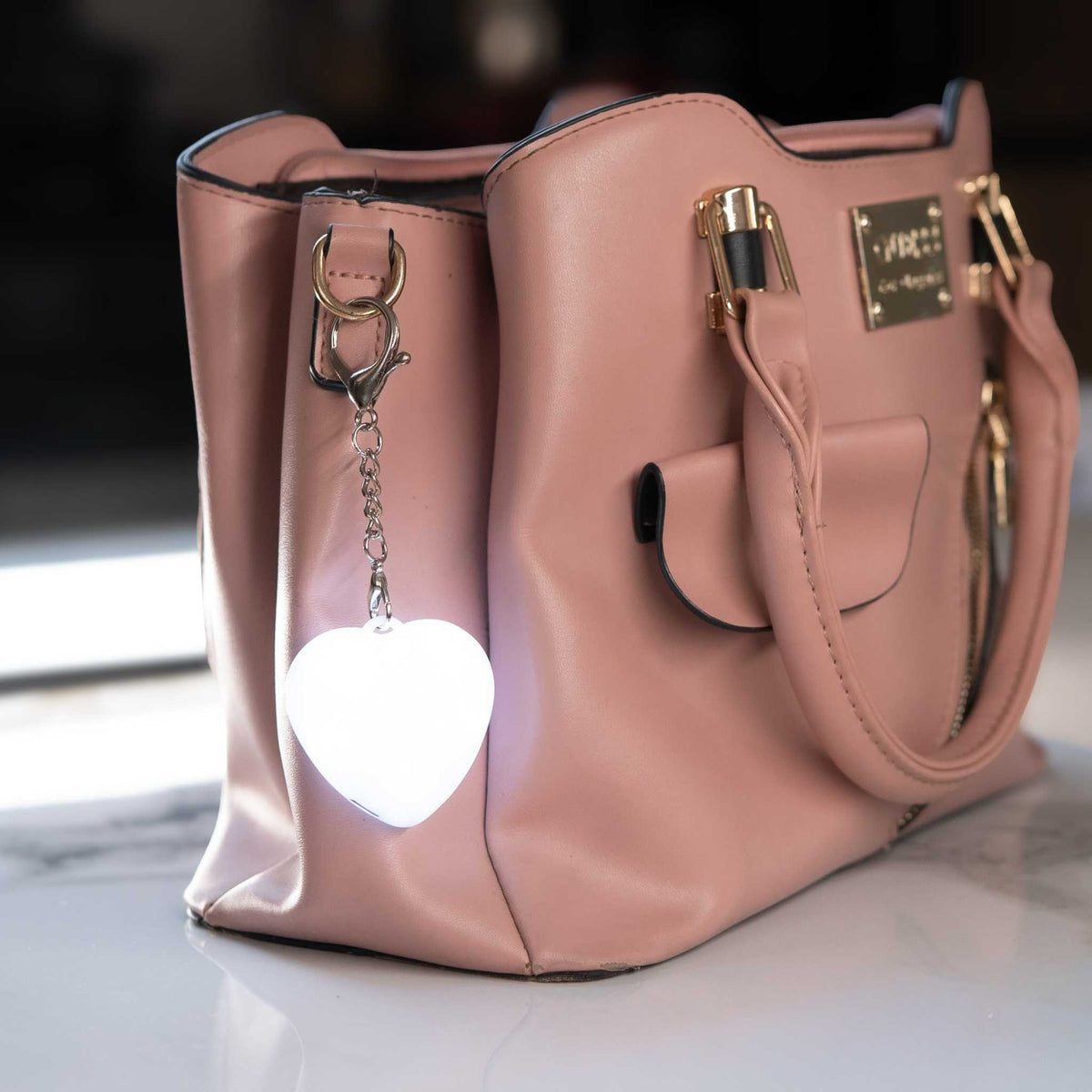 LumiHeart™ Motion Glow heart-shaped keychain light clipped to pink handbag glowing softly in low light